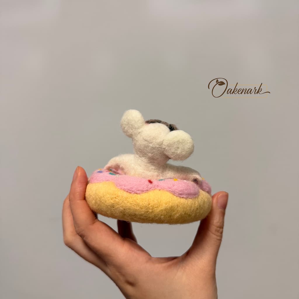Hand holding a small plush toy resembling a donut with a face on a plain background