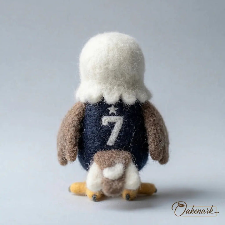 Felted toy eagle with a blue shirt and number 7 on a gray background, branded &