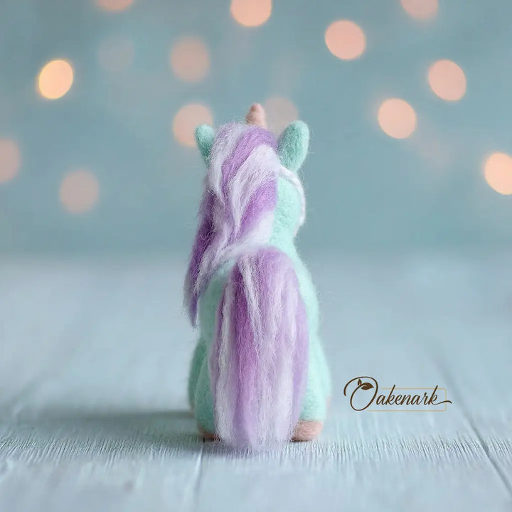 Small plush toy with pastel-colored fur on a light background, featuring the brand &