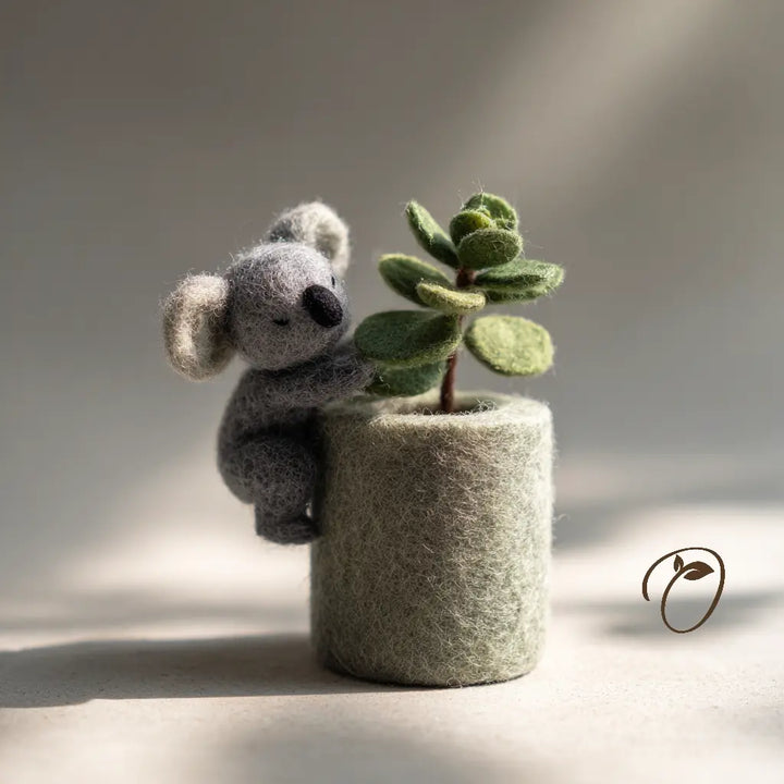 Felted koala holding a small plant in a felt pot on a neutral background
