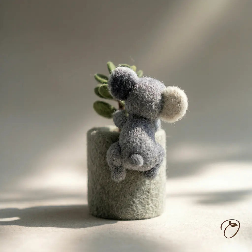 Gray fuzzy toy resembling a bear on a cylindrical gray base with a plant, against a neutral background.