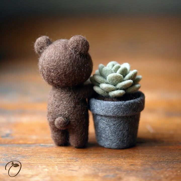 Small brown teddy bear hugging a potted succulent on a wooden surface