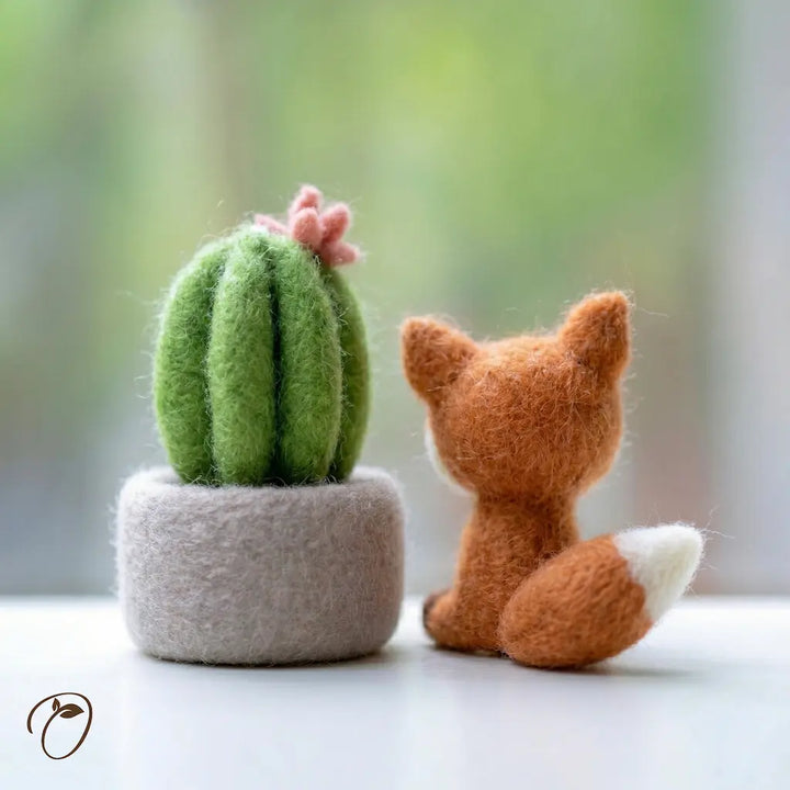Felted fox and cactus toy on a white surface with a blurred green background