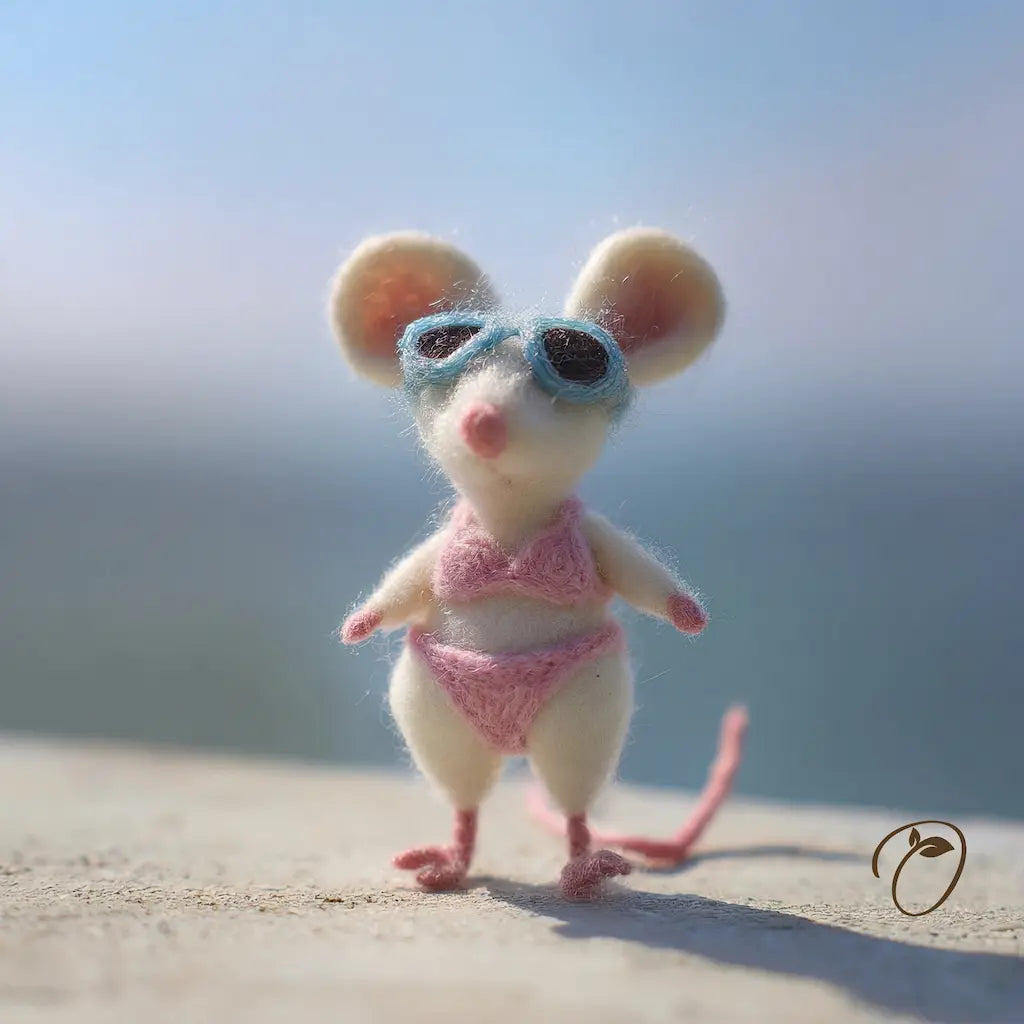 Toy mouse in a pink swimsuit and blue goggles on a blurred beach background