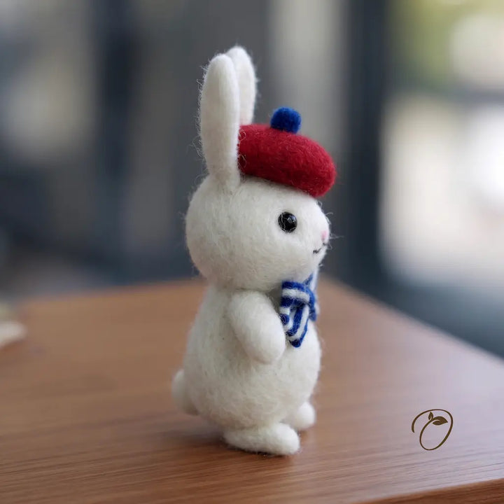 White rabbit plush toy wearing a red hat and blue scarf on a wooden surface