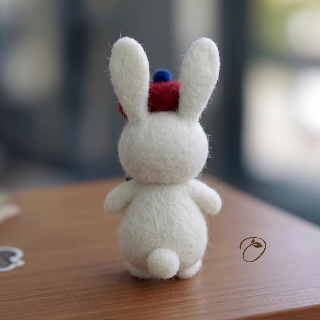 White plush toy rabbit with a red and blue hat on a wooden surface