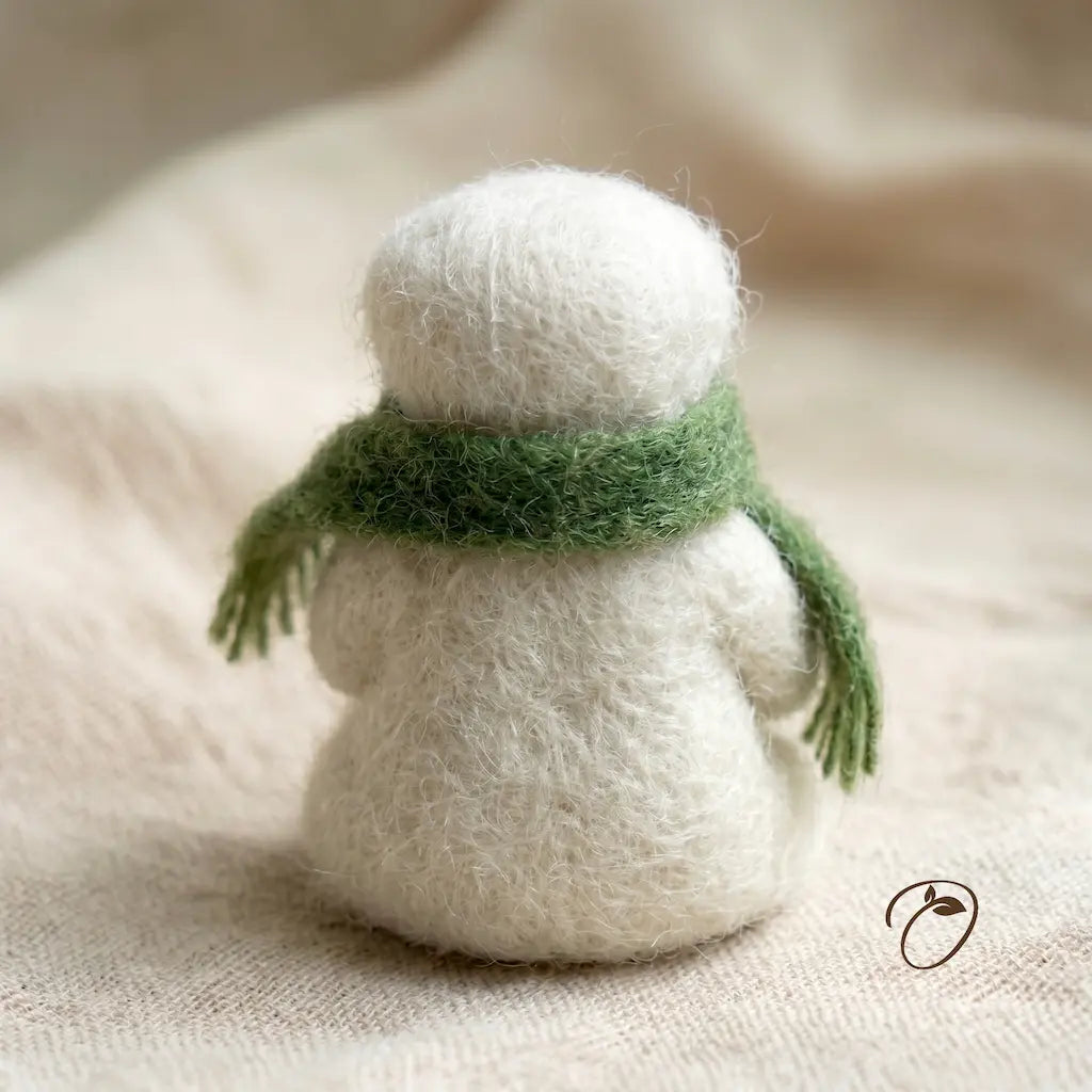 Small white knitted snowman with a green scarf on a beige fabric background