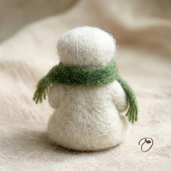 Small white knitted snowman with a green scarf on a beige fabric background