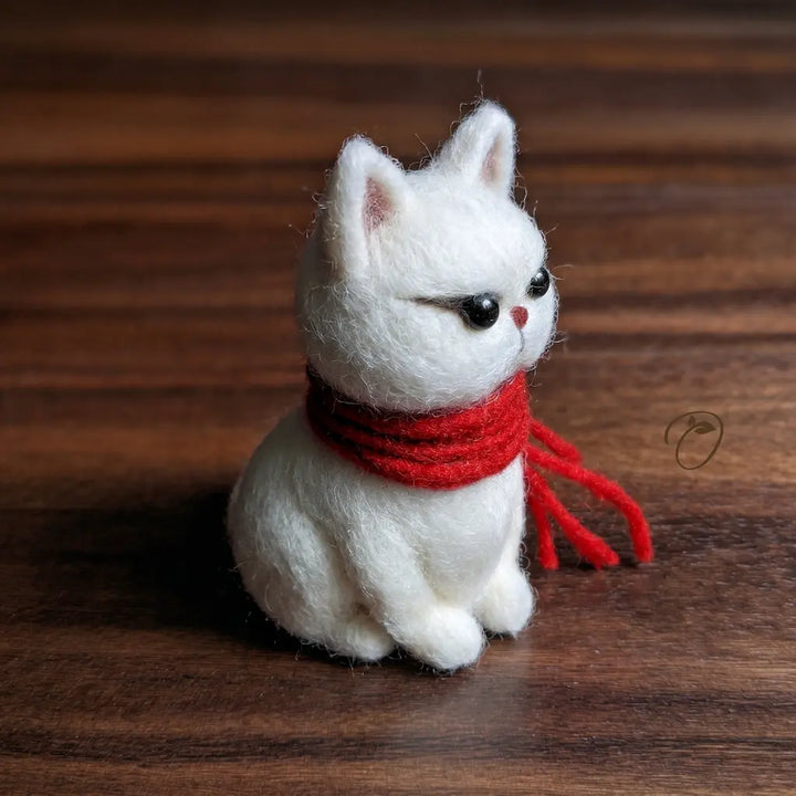 White cat figurine with a red scarf on a wooden surface