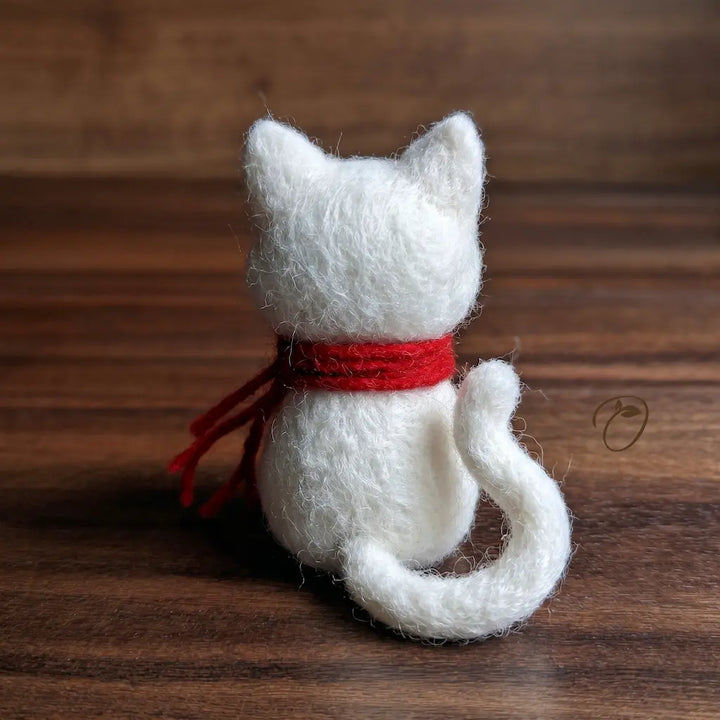 White knitted cat with a red ribbon on a wooden surface