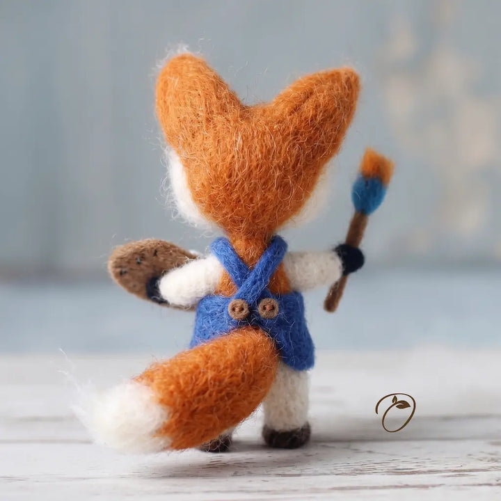 Toy fox with a blue apron and paintbrush on a wooden surface