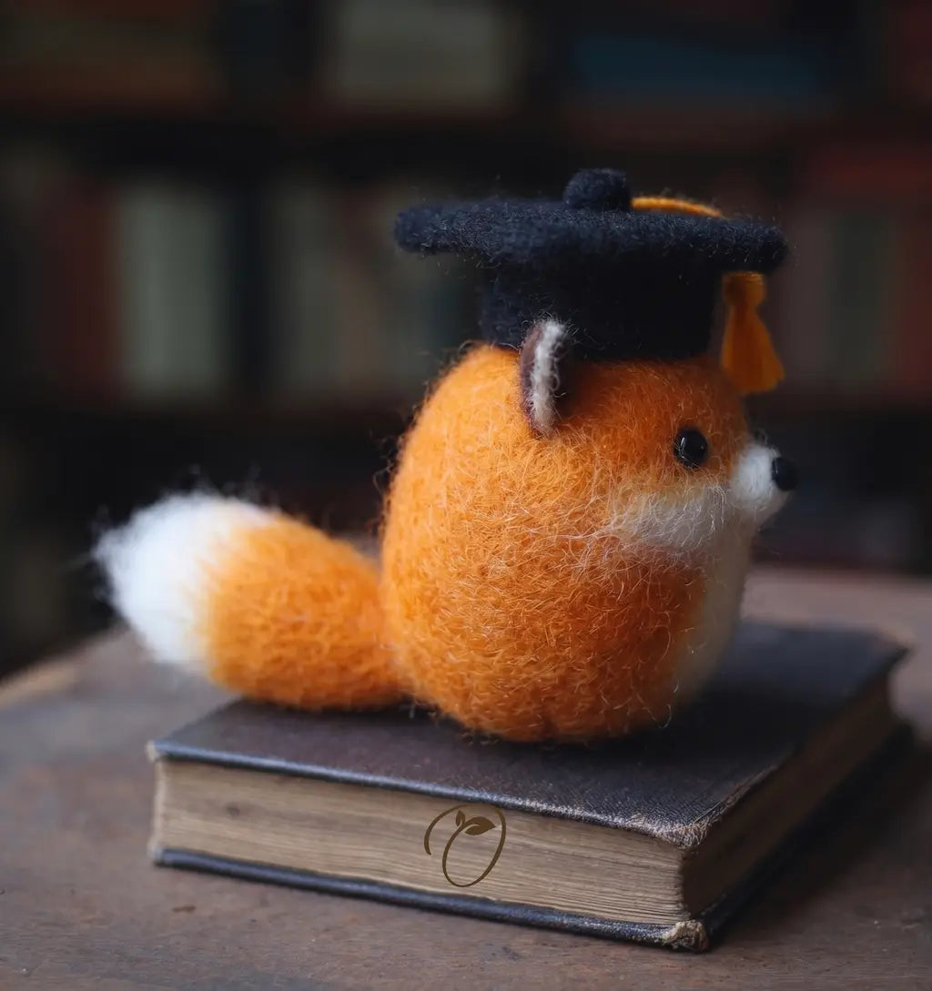Felted fox figurine wearing a graduation cap on a book