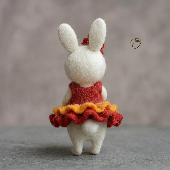 White rabbit toy wearing a red dress with an orange ruffled skirt on a neutral background