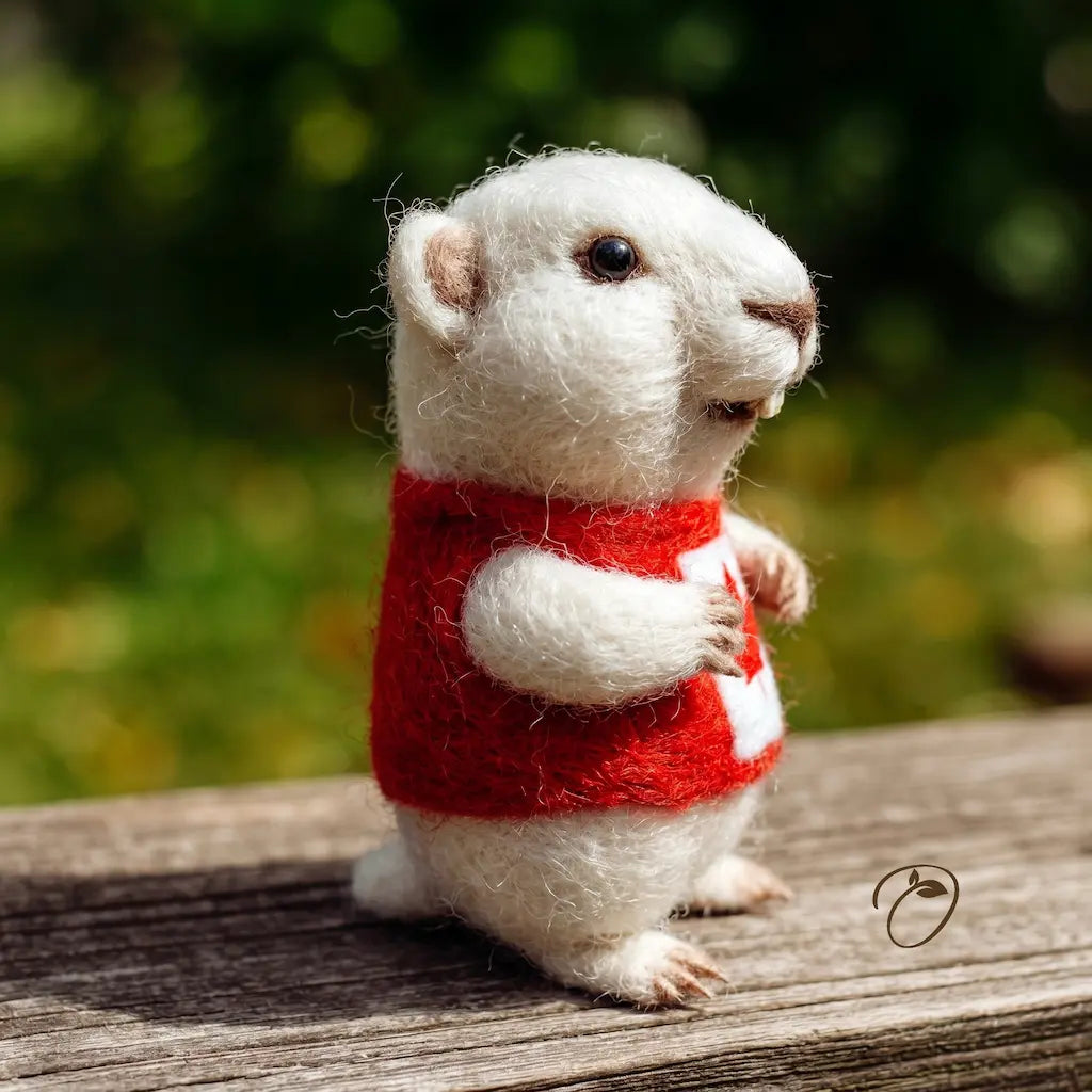 White animal figure wearing a red sweater on a wooden surface with a blurred natural background