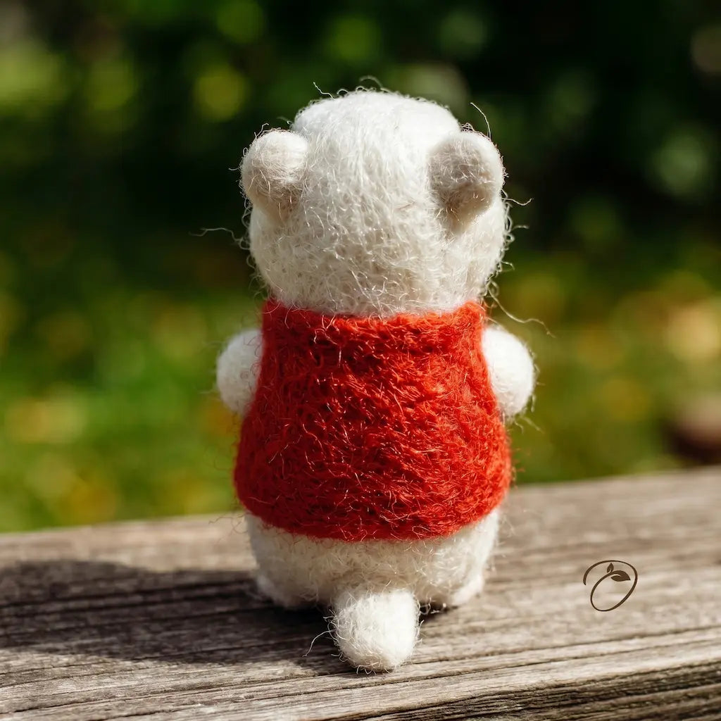 Small white animal figurine wearing a red sweater on a wooden surface with a blurred natural background