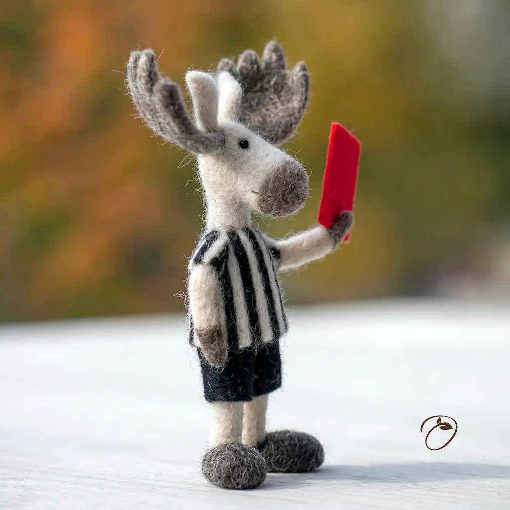 Toy moose in a referee outfit holding a red card against a blurred natural background