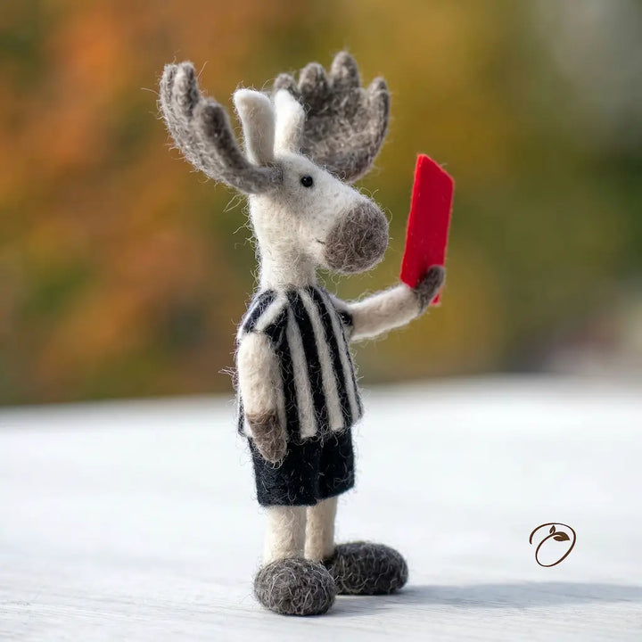 Toy moose in a referee outfit holding a red card against a blurred natural background