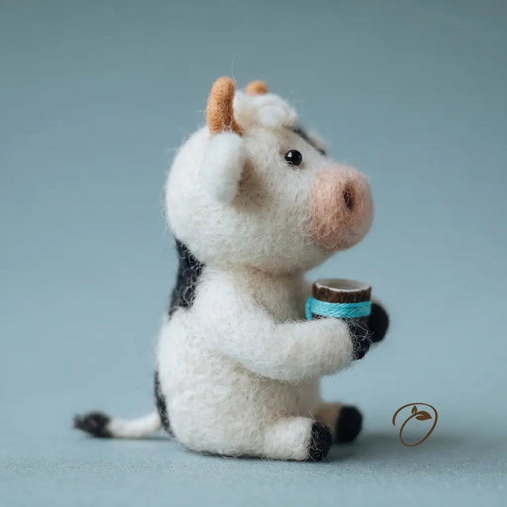 Felted cow toy holding a small barrel on a light blue background
