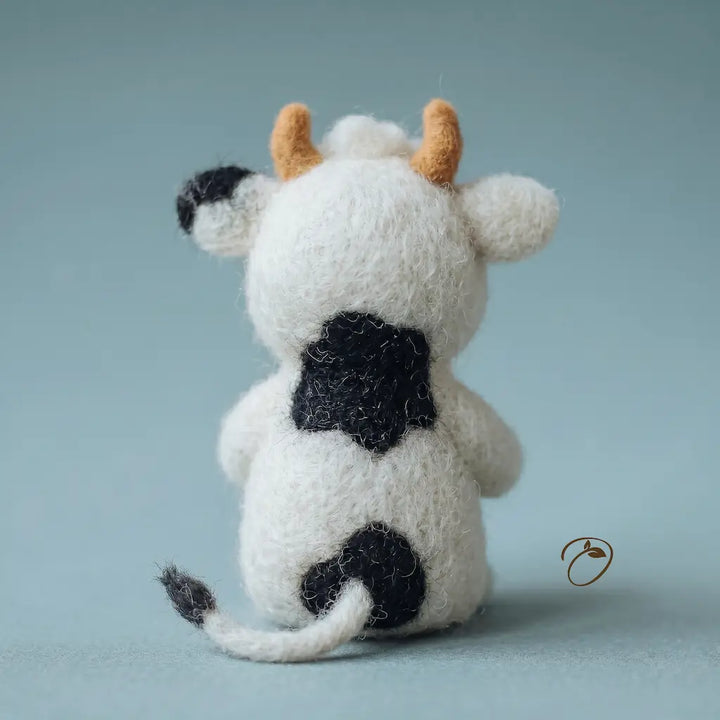 Small cow figurine with black spots and orange horns on a light blue background