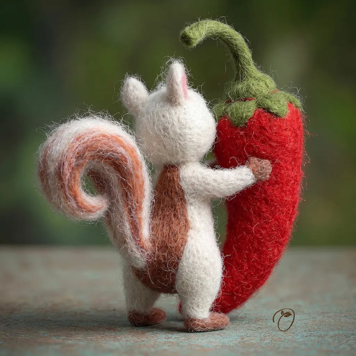 Felted sculpture of a squirrel holding a red chili pepper against a blurred natural background