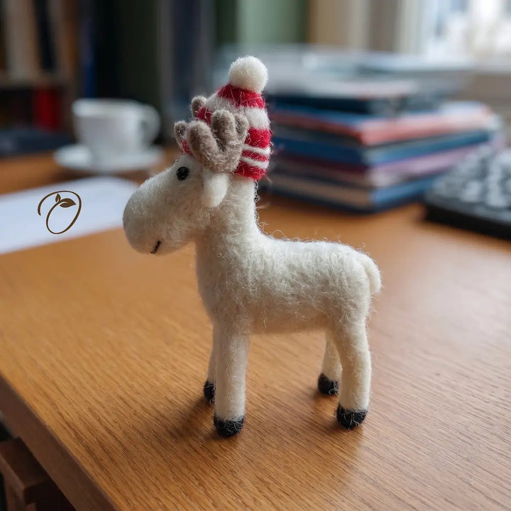 Small white stuffed reindeer with a red and white striped hat on a wooden surface.