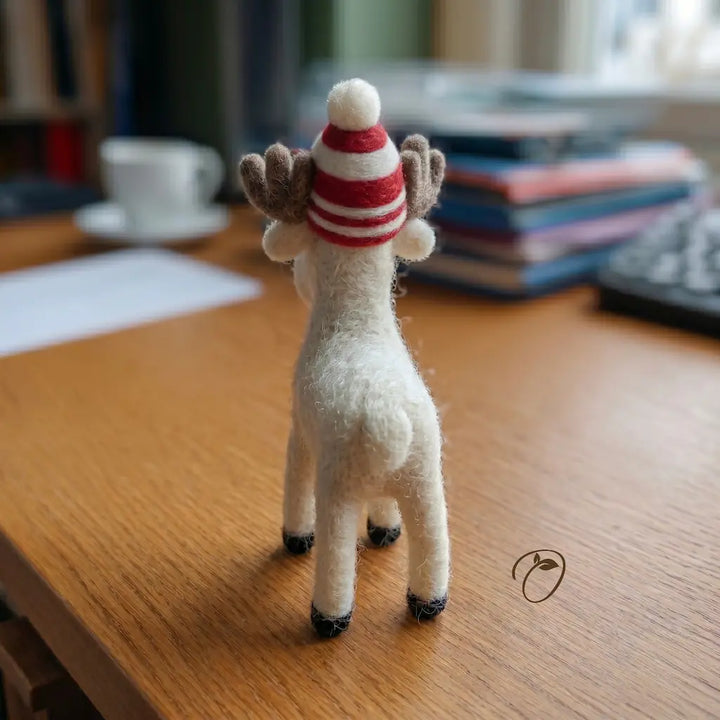 Small white reindeer figurine wearing a red and white striped hat on a wooden surface.