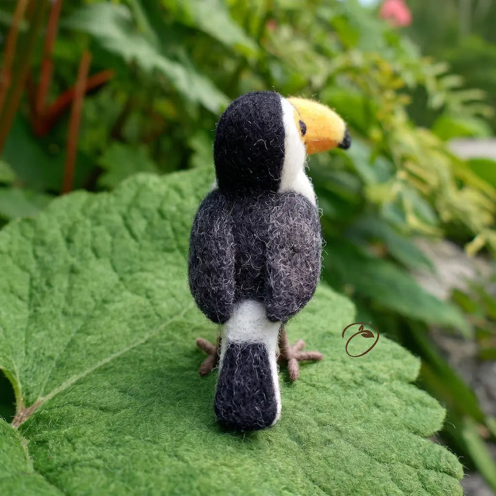 Felted toucan toy on a green leaf with a natural background