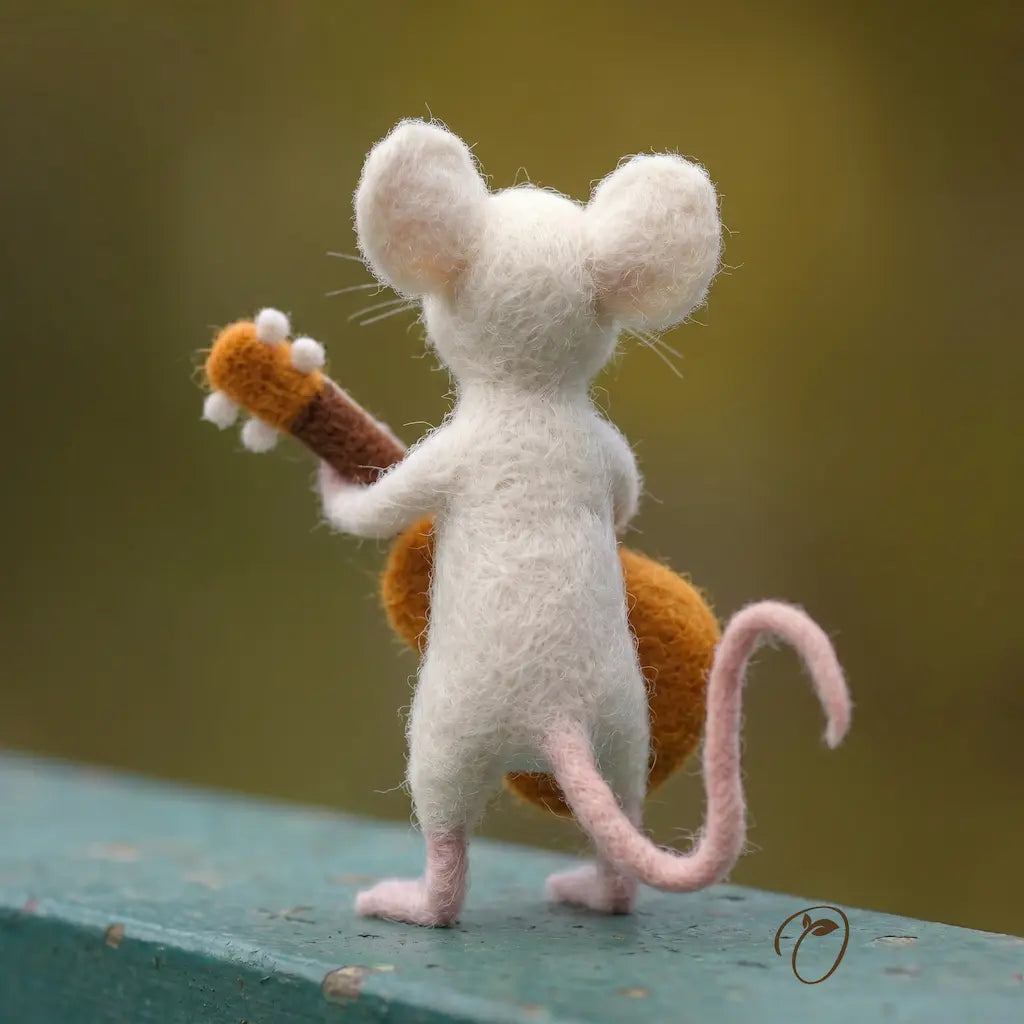 Felted mouse figurine holding a guitar on a green surface with a blurred background