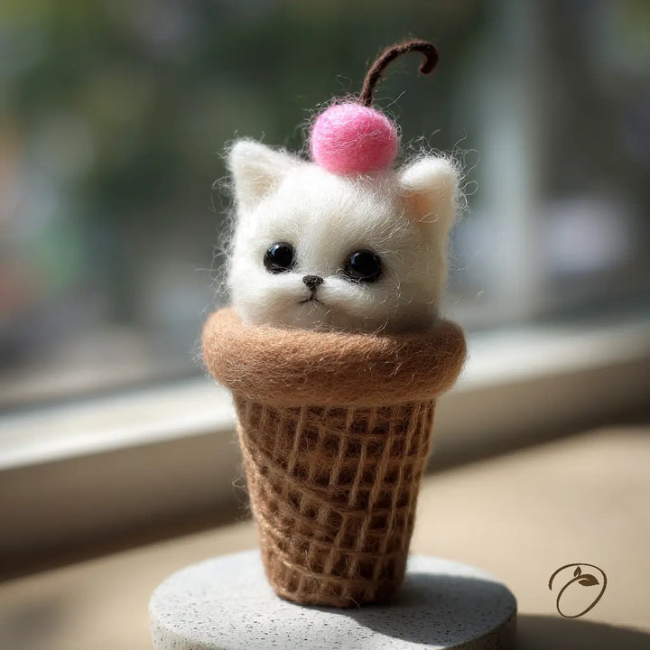 Toy cat in a waffle cone with a cherry on top, placed indoors.