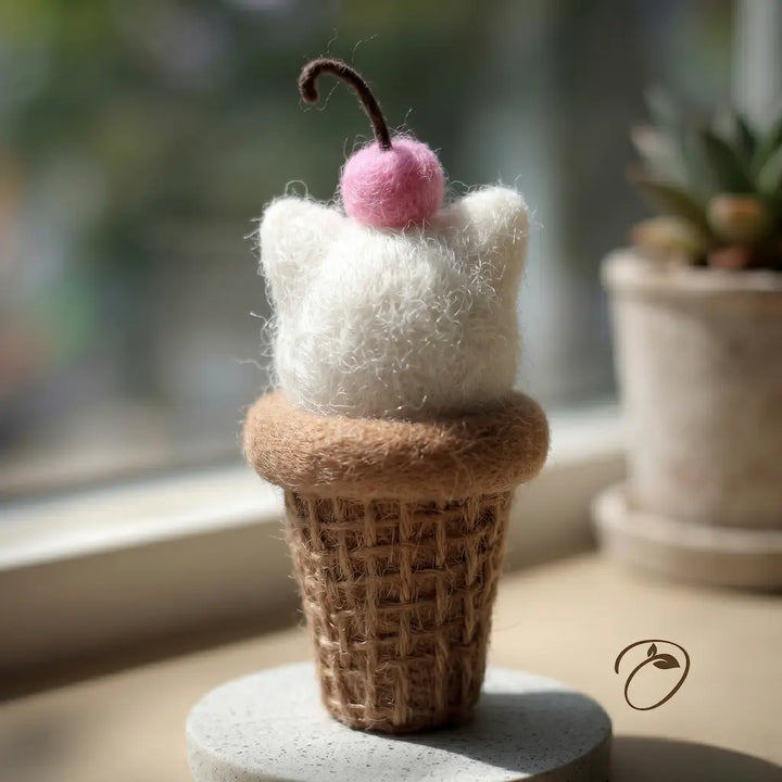 Felted ice cream cone with a cherry on top on a stone surface.
