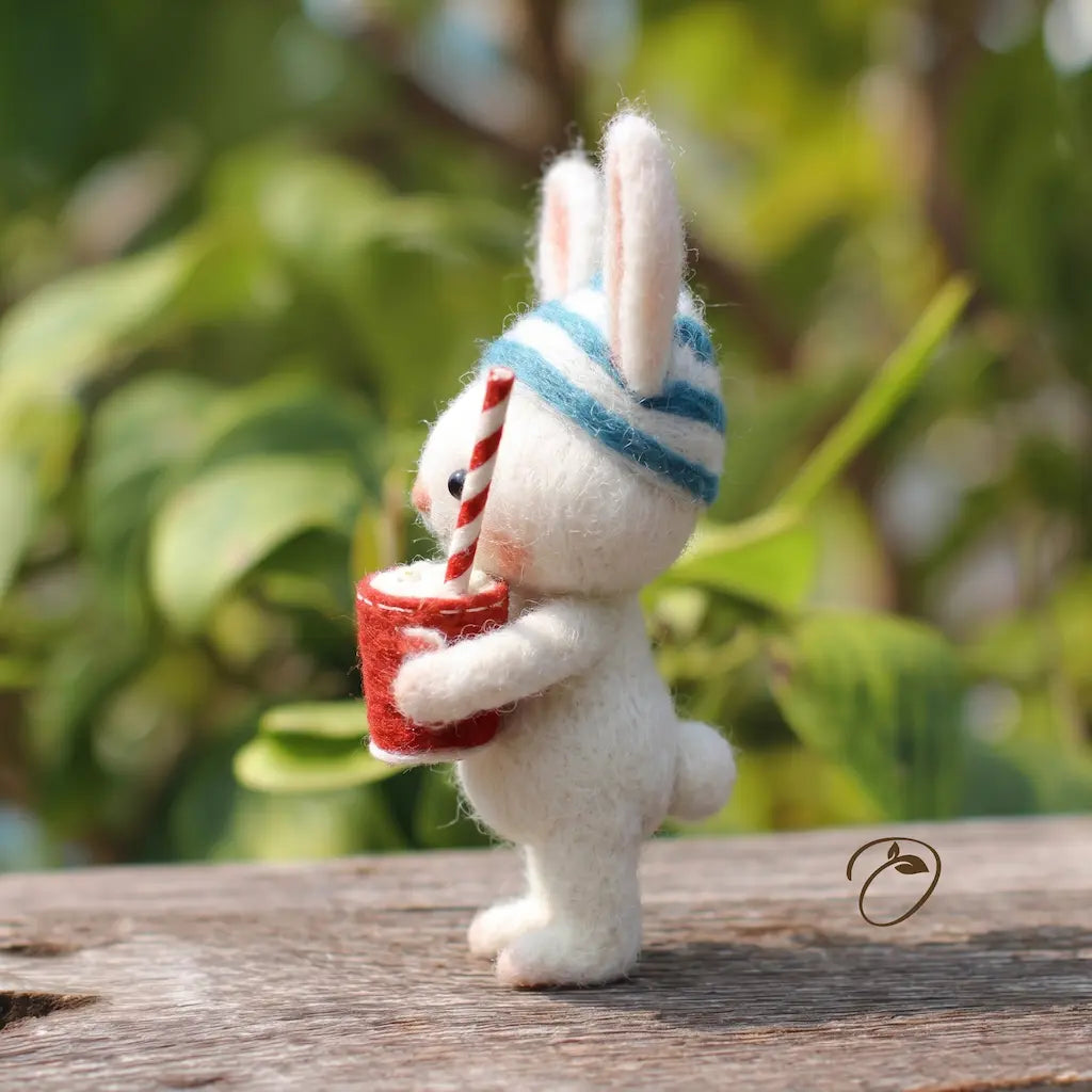 White bunny figurine with a striped hat and red cup against a blurred green background