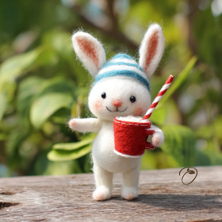 Toy rabbit wearing a striped hat and holding a red cup with a straw against a blurred green background