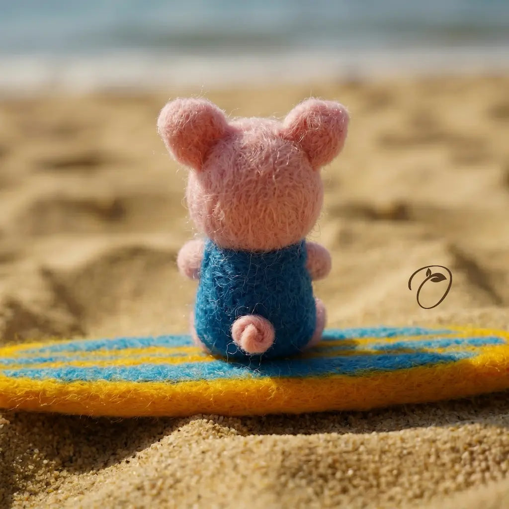 Small pink toy mouse in a blue outfit sitting on a yellow and blue striped surfboard on a sandy beach.