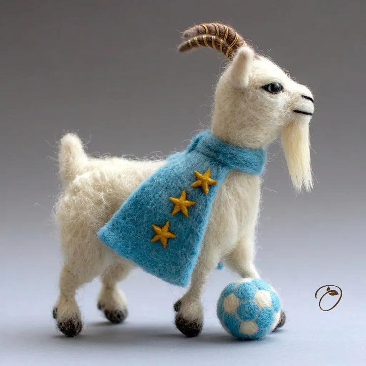 Toy goat wearing a blue coat with gold stars and a blue ball on a gray background