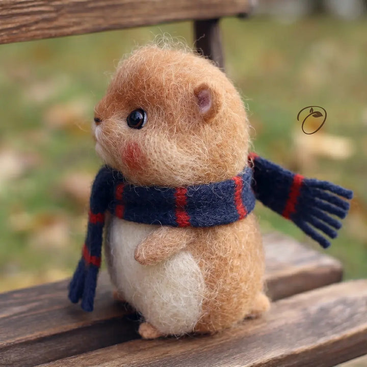 Small animal figurine wearing a scarf and gloves on a wooden surface with a blurred natural background