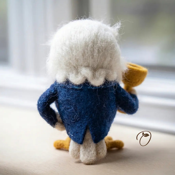 Small plush toy resembling a character with a blue coat and white hair on a light surface.