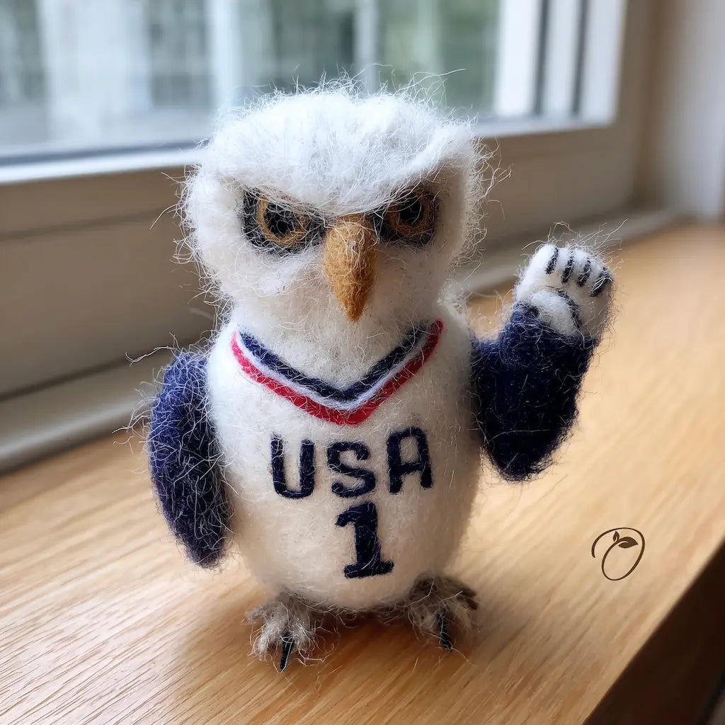 Felted owl figurine wearing a USA jersey on a wooden surface.