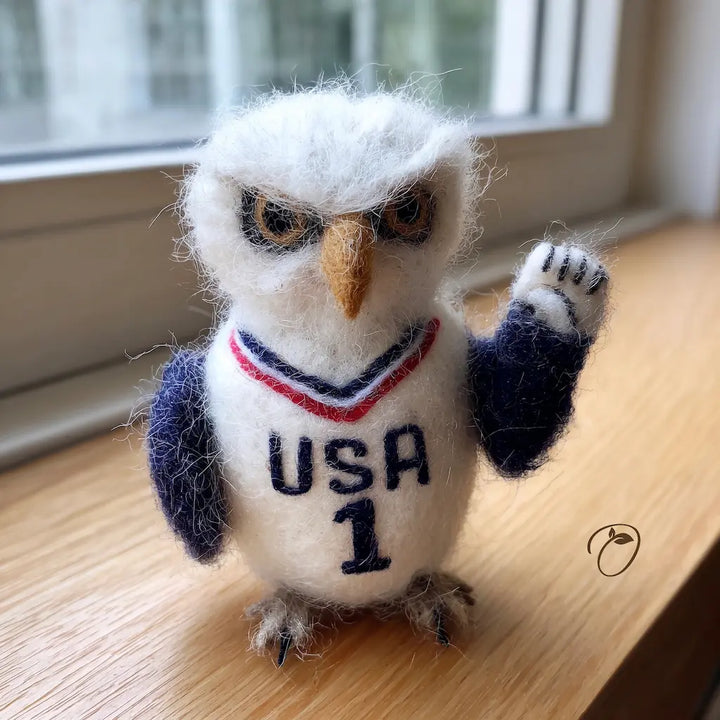 Felted owl figurine wearing a USA jersey on a wooden surface.