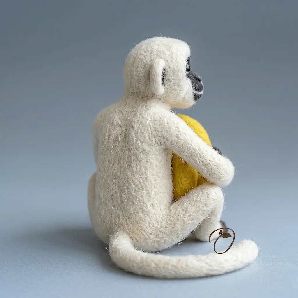 White monkey plush toy holding a yellow ball on a gray background