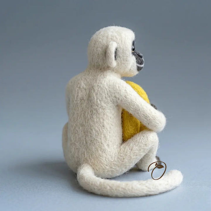 White monkey plush toy holding a yellow ball on a gray background