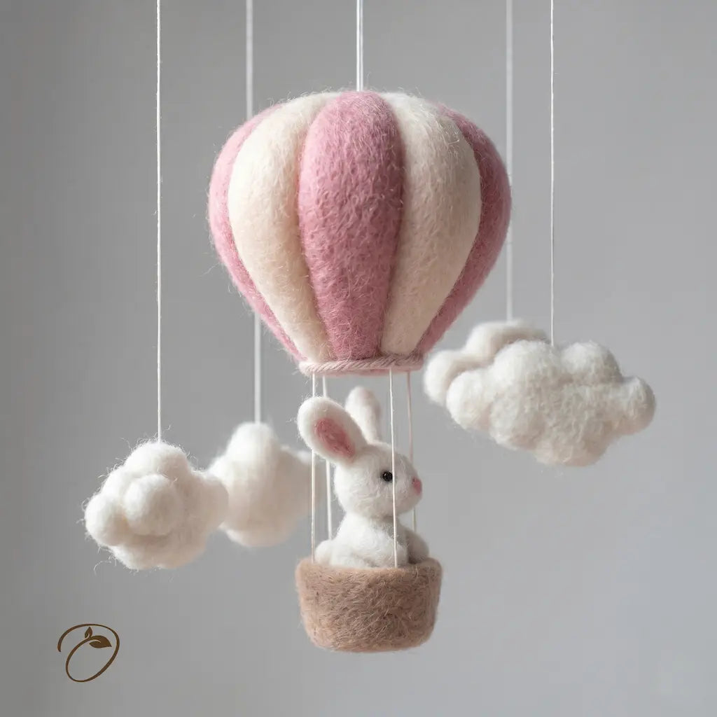 Felted pink and white hot air balloon with a rabbit inside, hanging against a gray background.