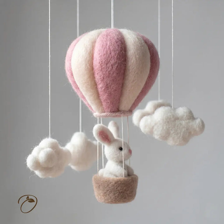 Felted pink and white hot air balloon with a rabbit inside, hanging against a gray background.