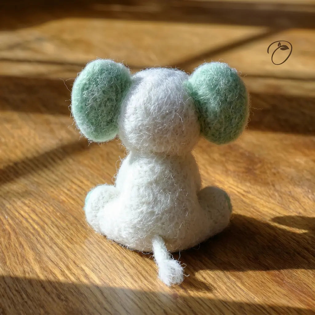 Small white and green plush toy on a wooden surface