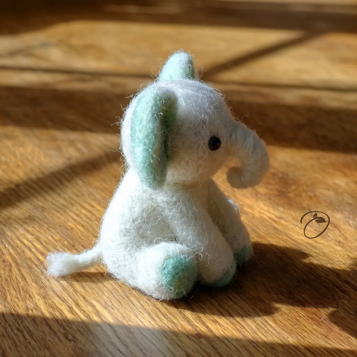 Small white elephant plush toy with green feet and trunk on a wooden surface