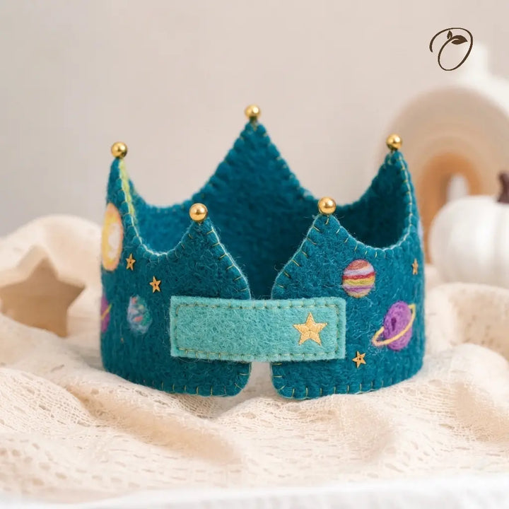 Teal felt crown with space-themed decorations on a soft beige surface