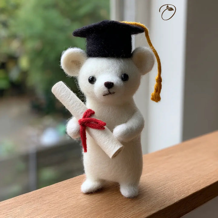 White teddy bear wearing a graduation cap and holding a diploma on a wooden surface.