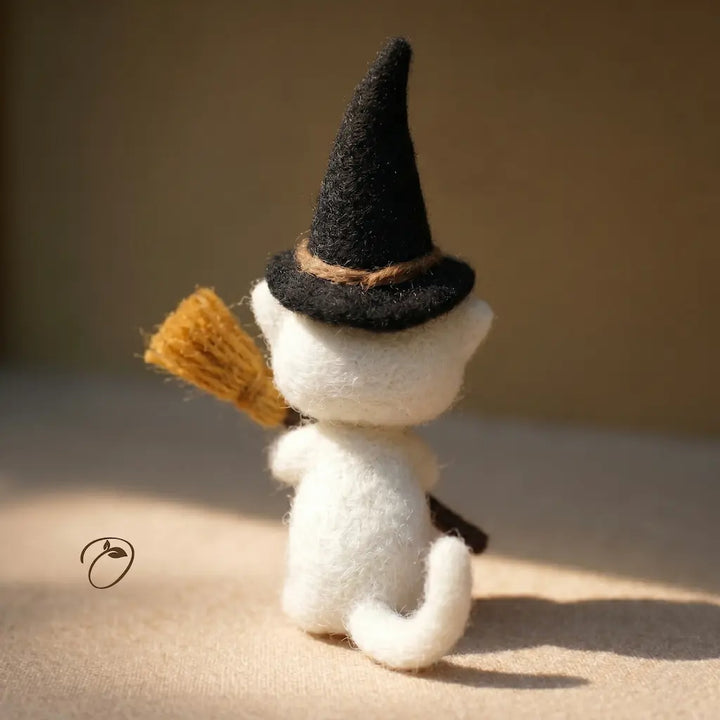 Toy cat wearing a witch hat and holding a broomstick on a beige background