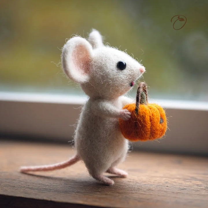 Felted mouse holding a small pumpkin on a wooden surface with a blurred background