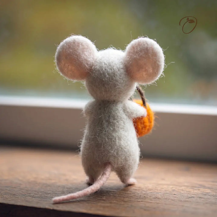 Felted mouse figurine holding an orange on a wooden surface with a blurred natural background