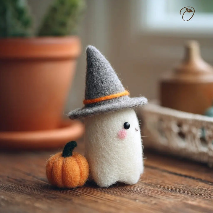 Small plush ghost toy with a witch hat and pumpkin on a wooden surface, with a blurred indoor background.